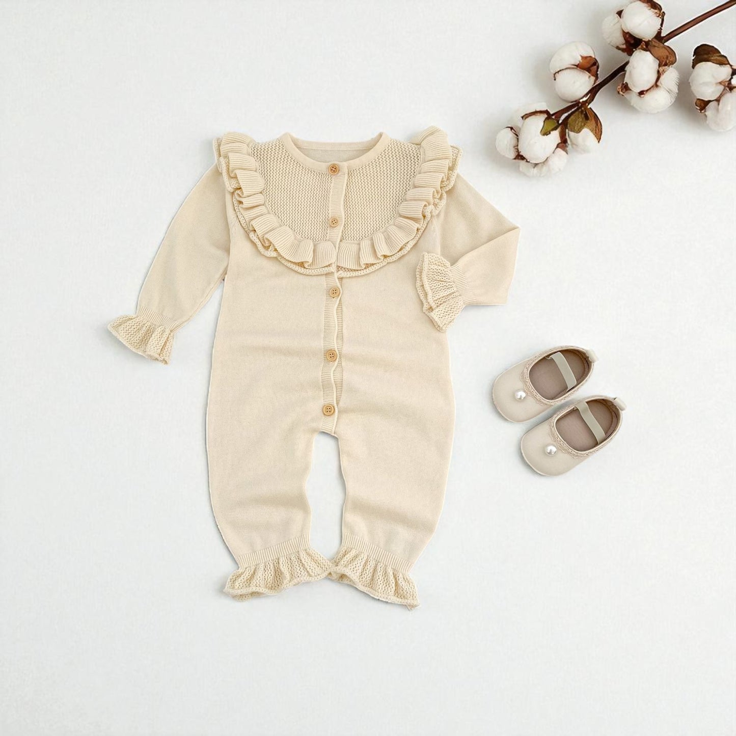 Cream baby romper with ruffled details on a light grey background with cotton branches.
