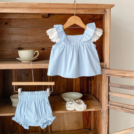 Light blue top with ruffled sleeves hanging on a wooden shelf with matching bloomers and shoes.