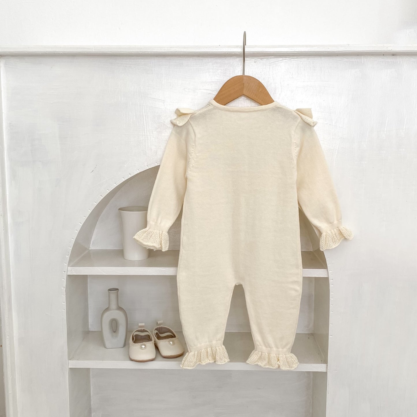 Back of baby romper with ruffled sleeves and legs hanging on a wooden hanger against a white background.