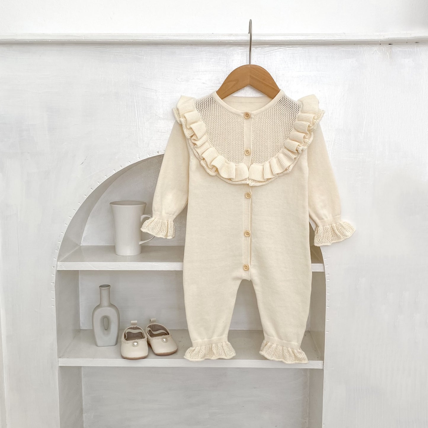 Cream baby romper with ruffles on a wooden hanger against a white background.