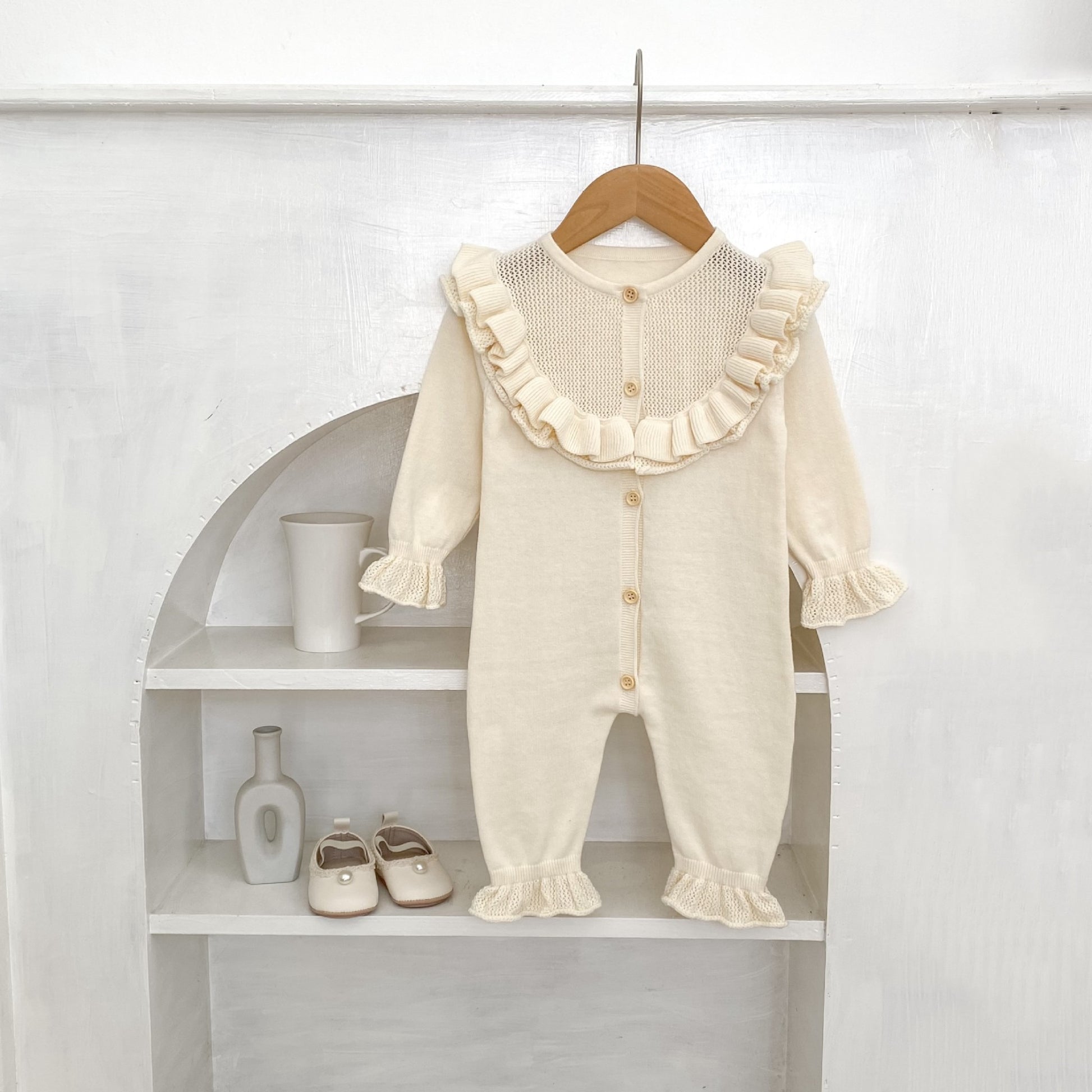 Cream baby romper with ruffles on a wooden hanger against a white background.