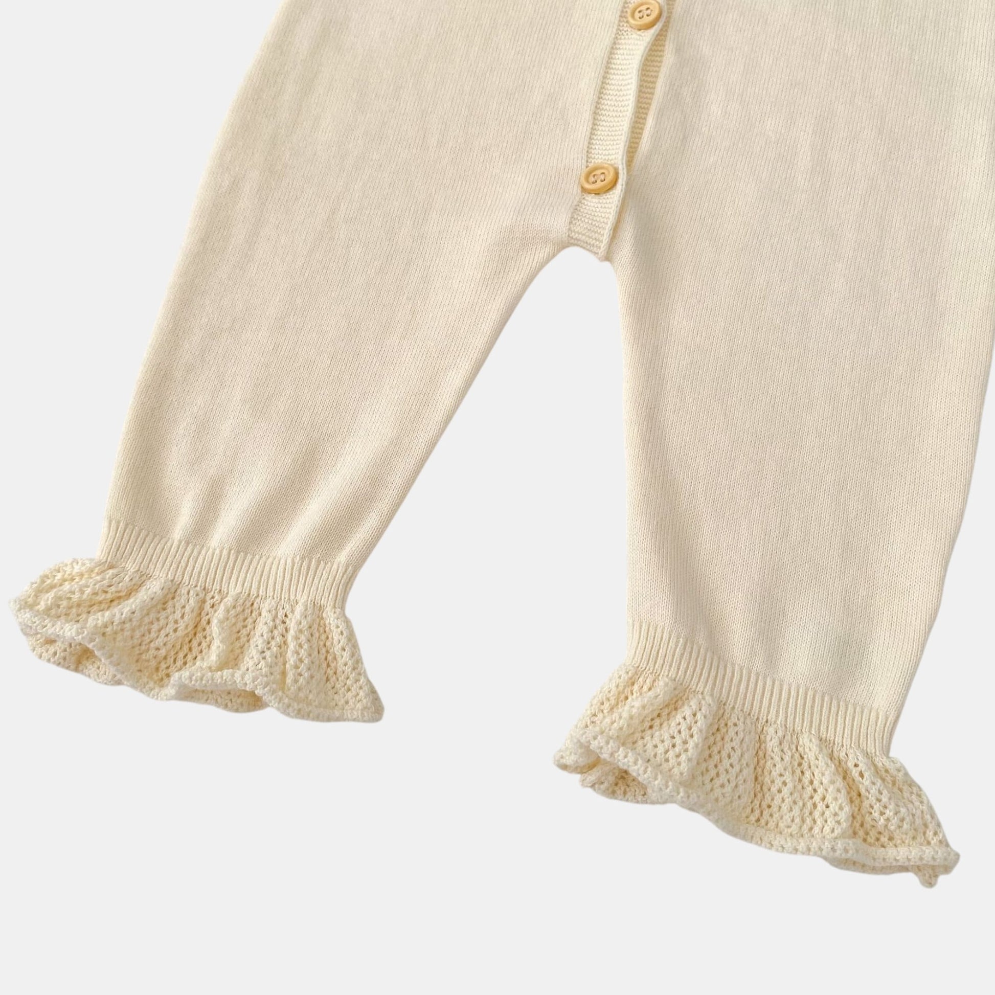Cream knitted baby romper legs with ruffled cuffs on a light grey background