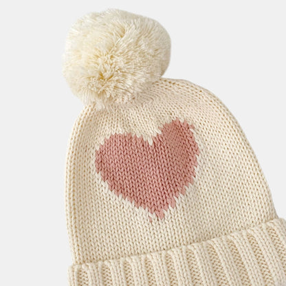 Knitted cream beanie with a heart design and pom-pom on a white background