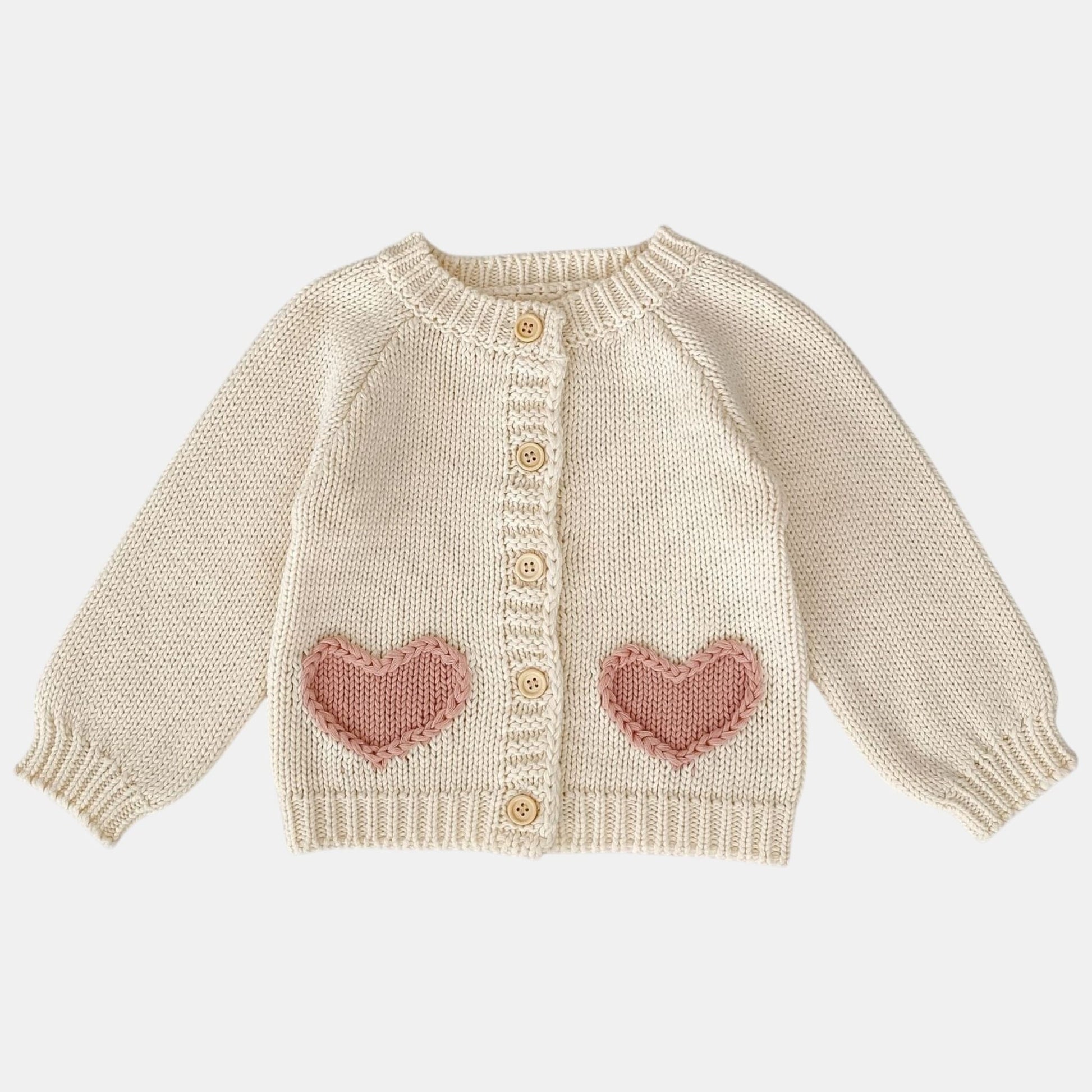 Knitted cream baby cardigan with pink heart patterns on a white background