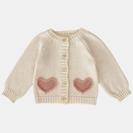 Knitted cream baby cardigan with pink heart patterns on a white background
