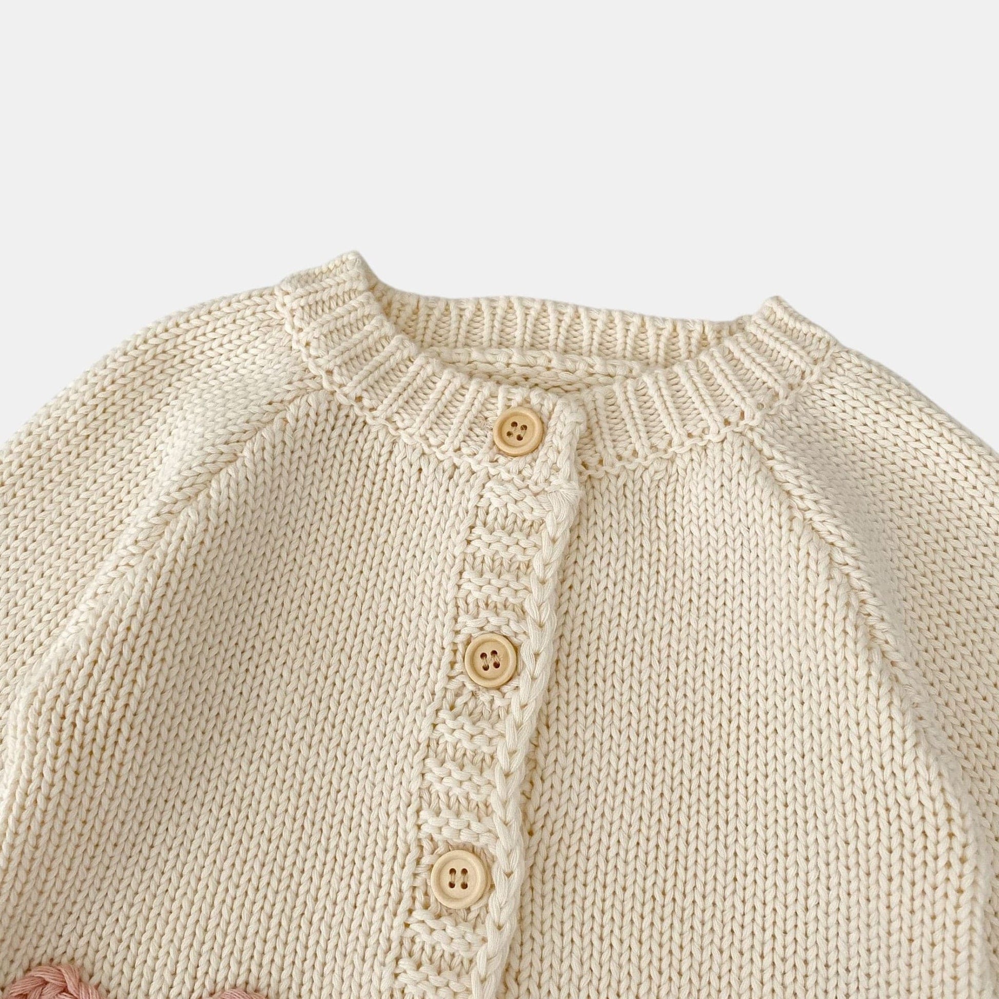 Close-up of a cream knitted cardigan with button details on a light grey background