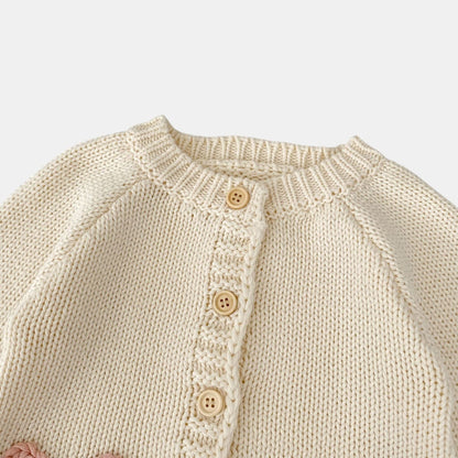 Close-up of a cream knitted cardigan with button details on a light grey background
