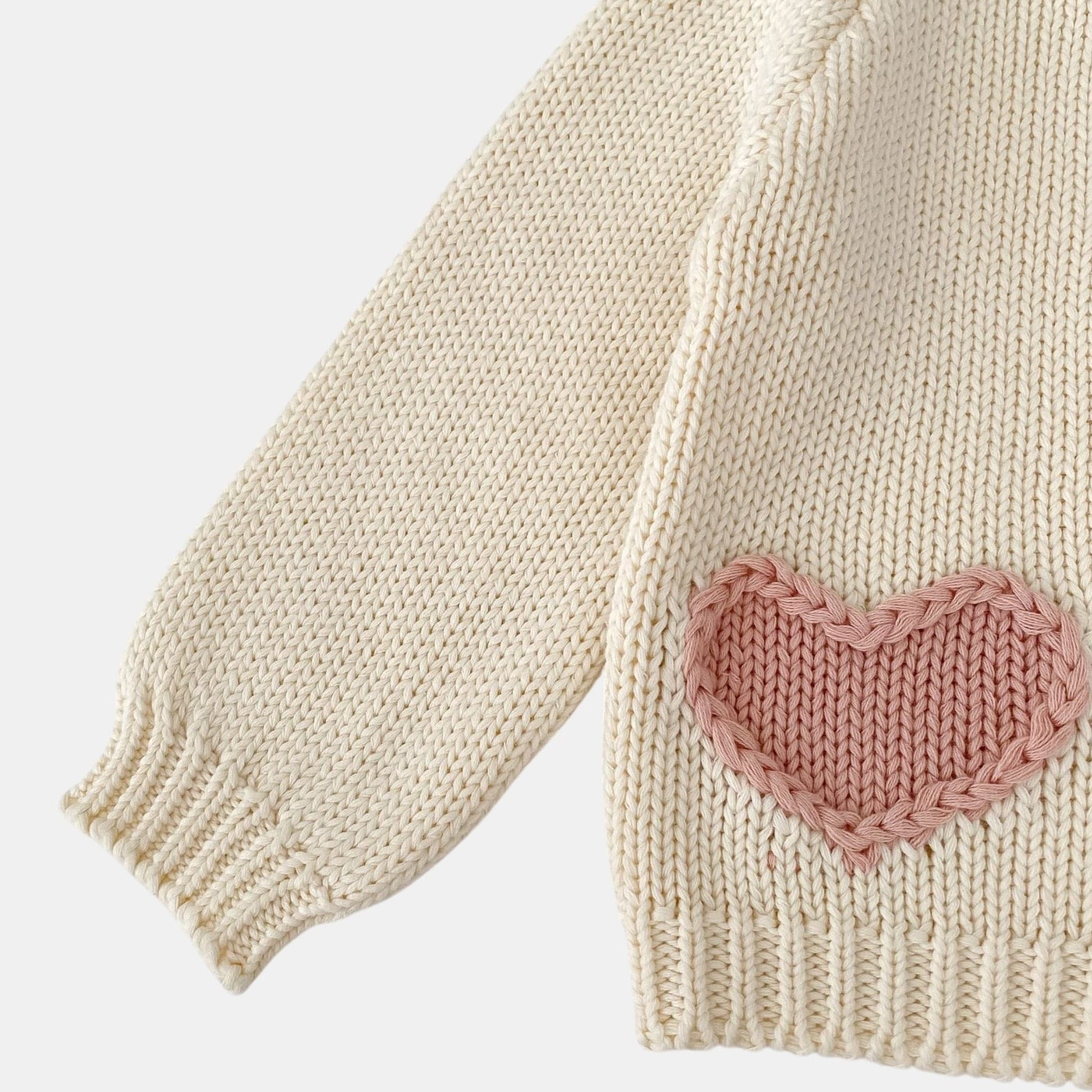 Cream knitted sweater with a pink heart patch on a light grey background