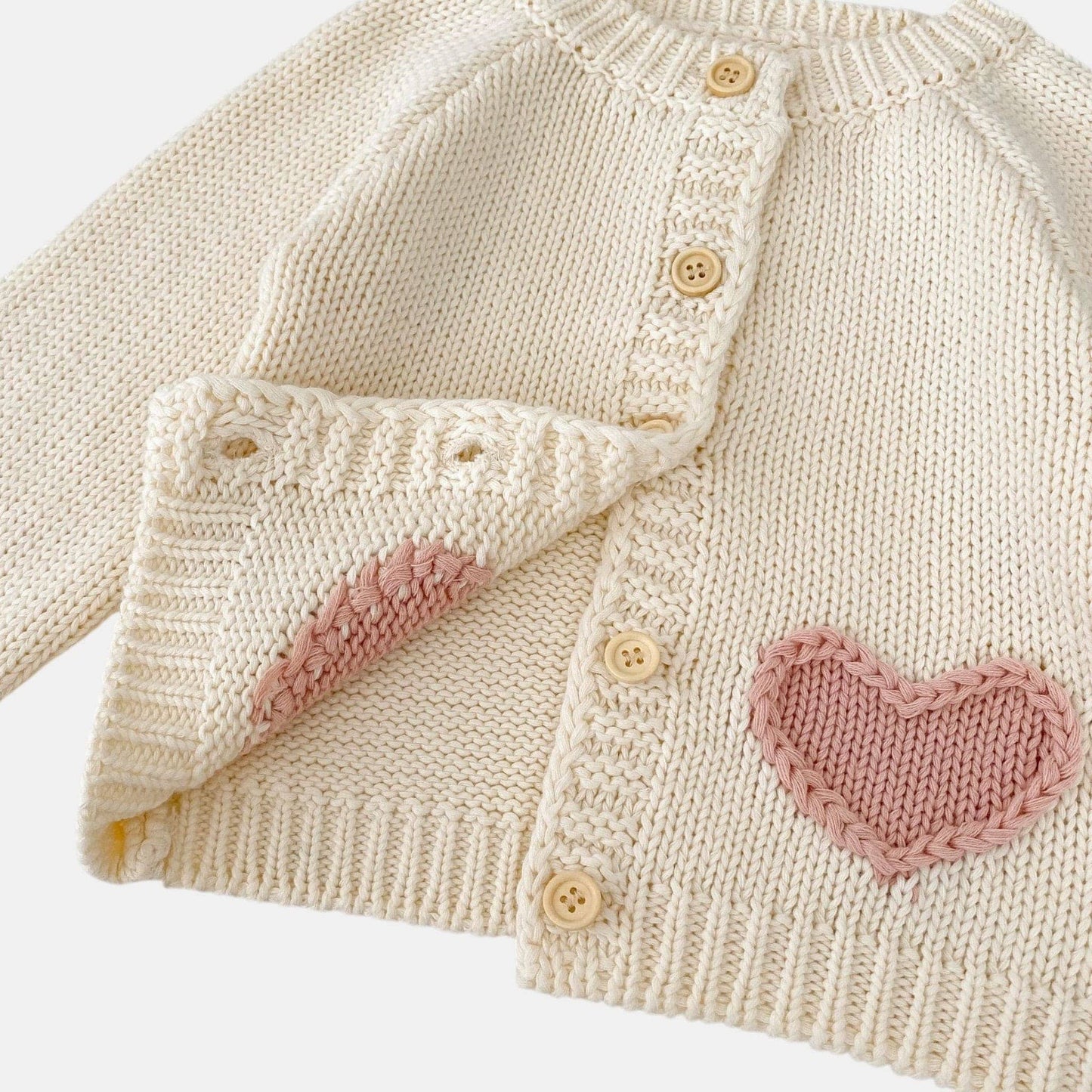 Knitted cream baby cardigan with pink heart patterns on a light background