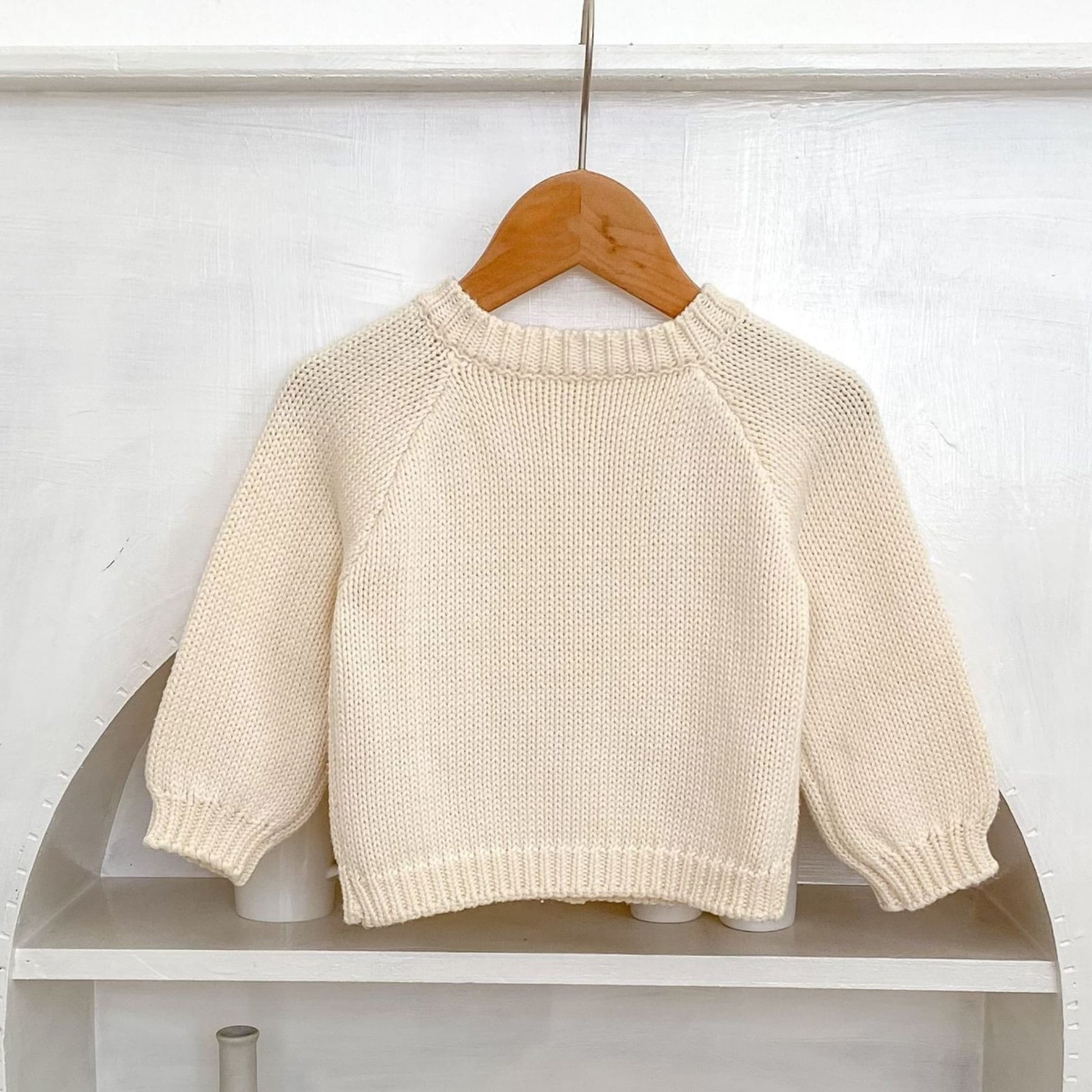 Back of cream knit baby cardigan on a wooden hanger against a white background