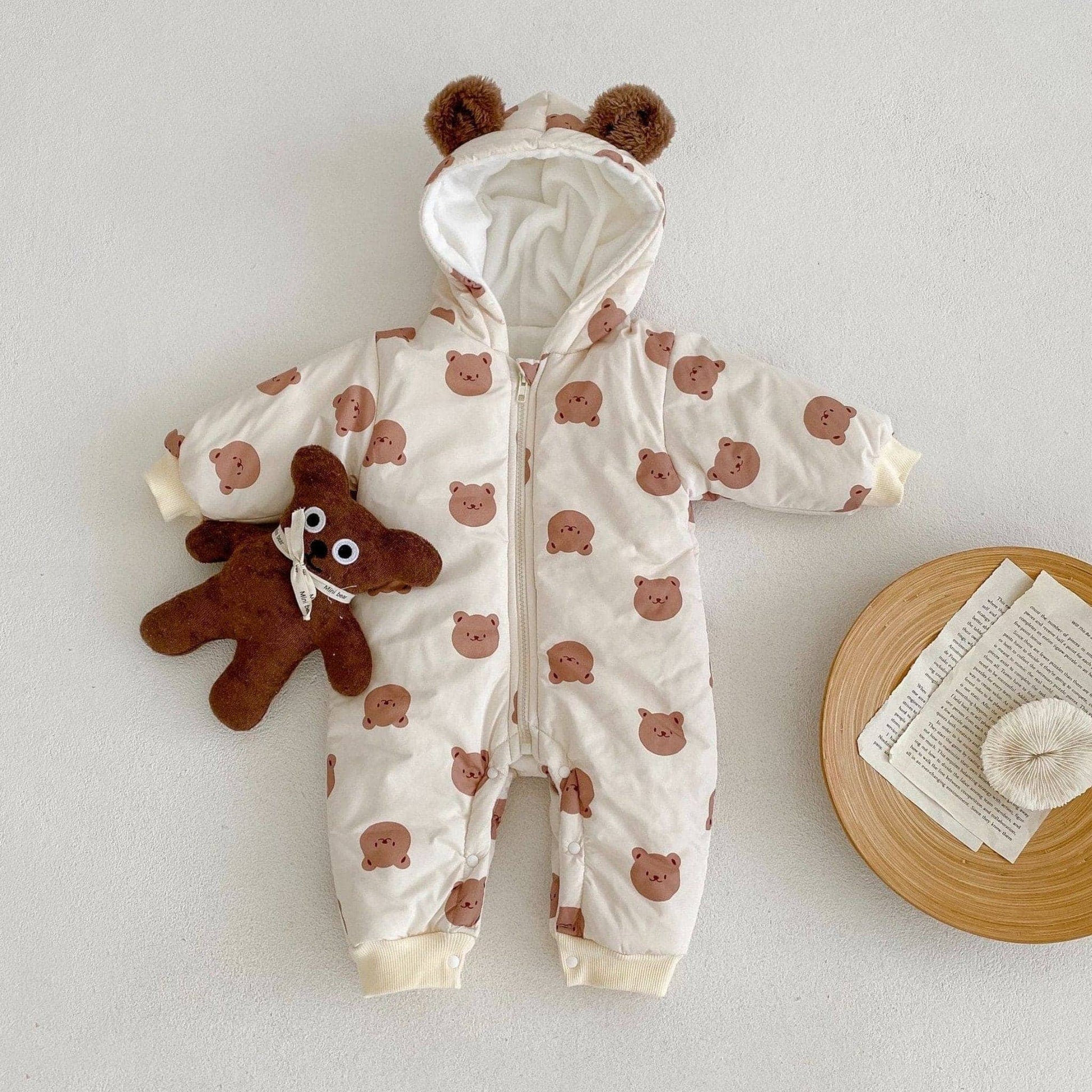 Baby pramsuit with bear pattern and teddy bear toy on a light background