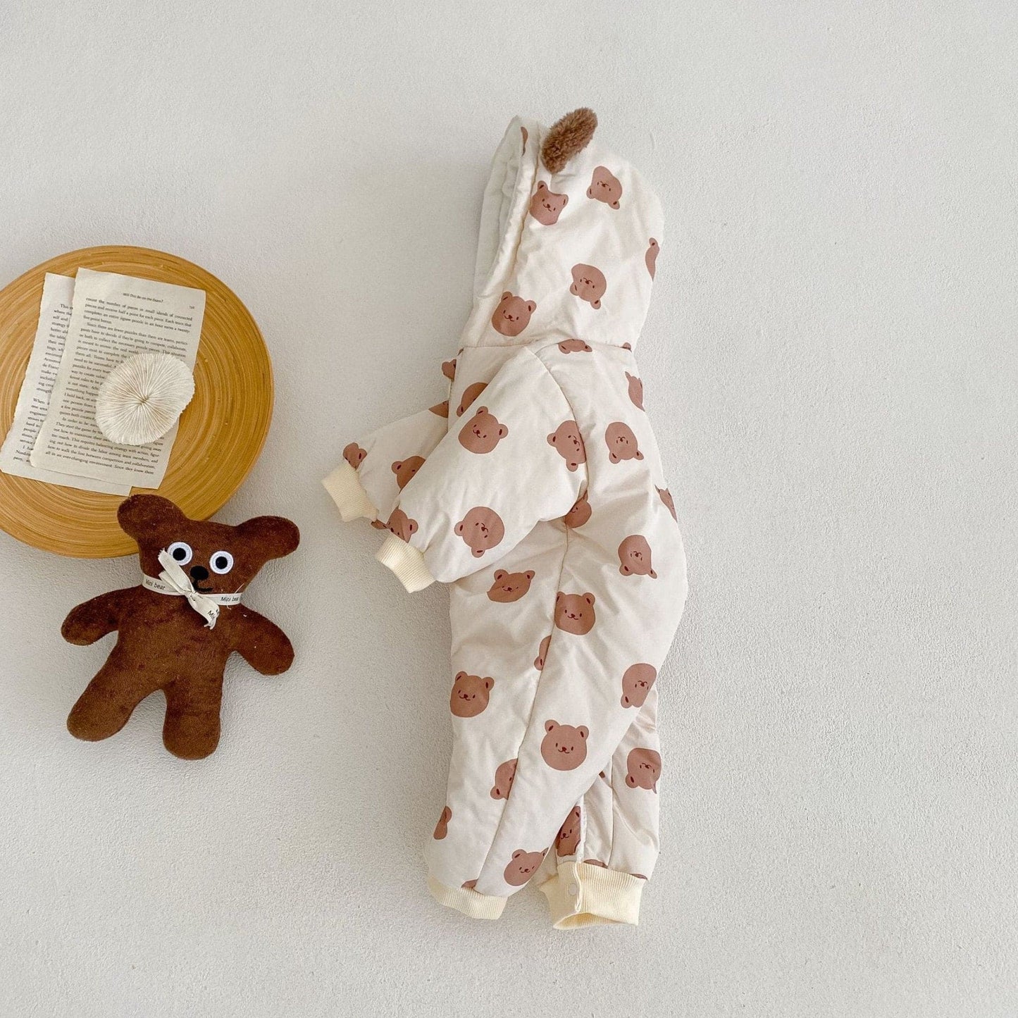 Baby pramsuit with bear pattern and teddy bear toy on a light background